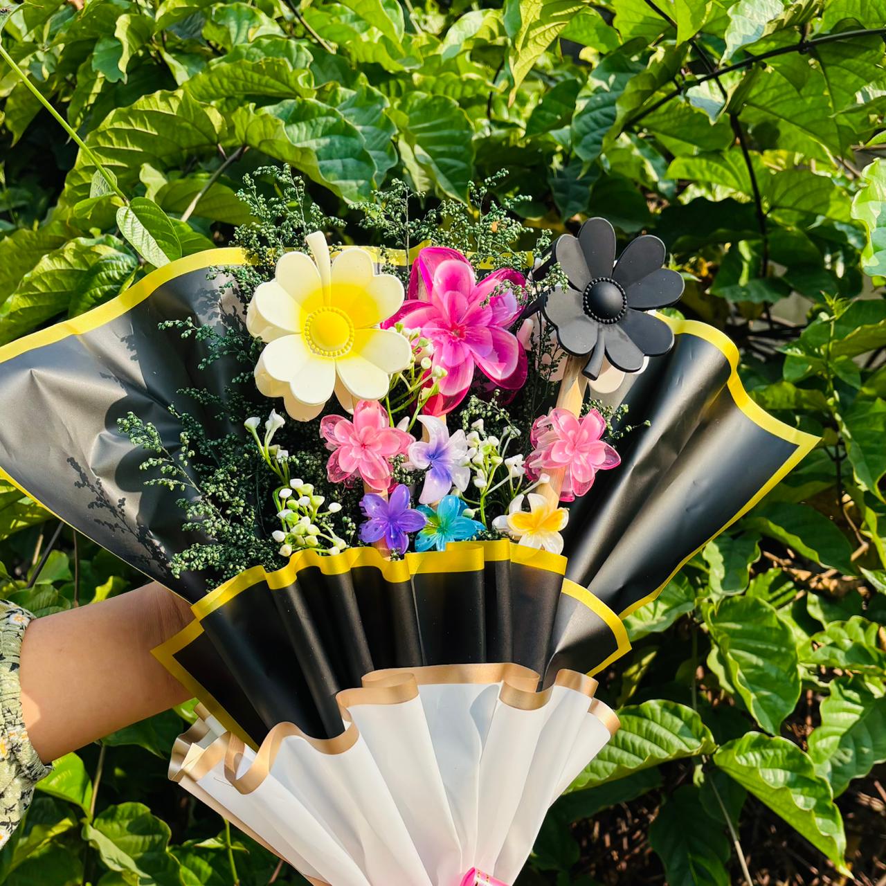 Black and yellow fan with colorful flowers held against a green leafy background Limited Edition Saar Beauty Hair Clutcher Bouquet – Unique floral gift with 9 colorful hair claw clips beautifully wrapped for women and girls.