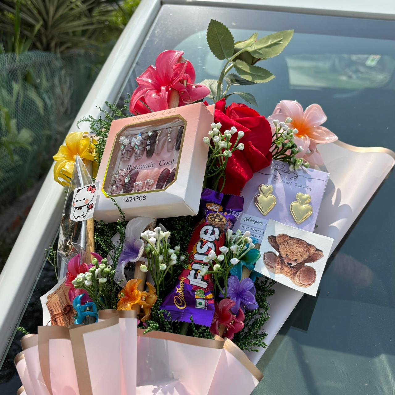 Gift basket with flowers, candies, and small items on a car hood Pinterest-inspired Saar Beauty Forever Gift Bouquet with hair claws, nail box, and jewelry