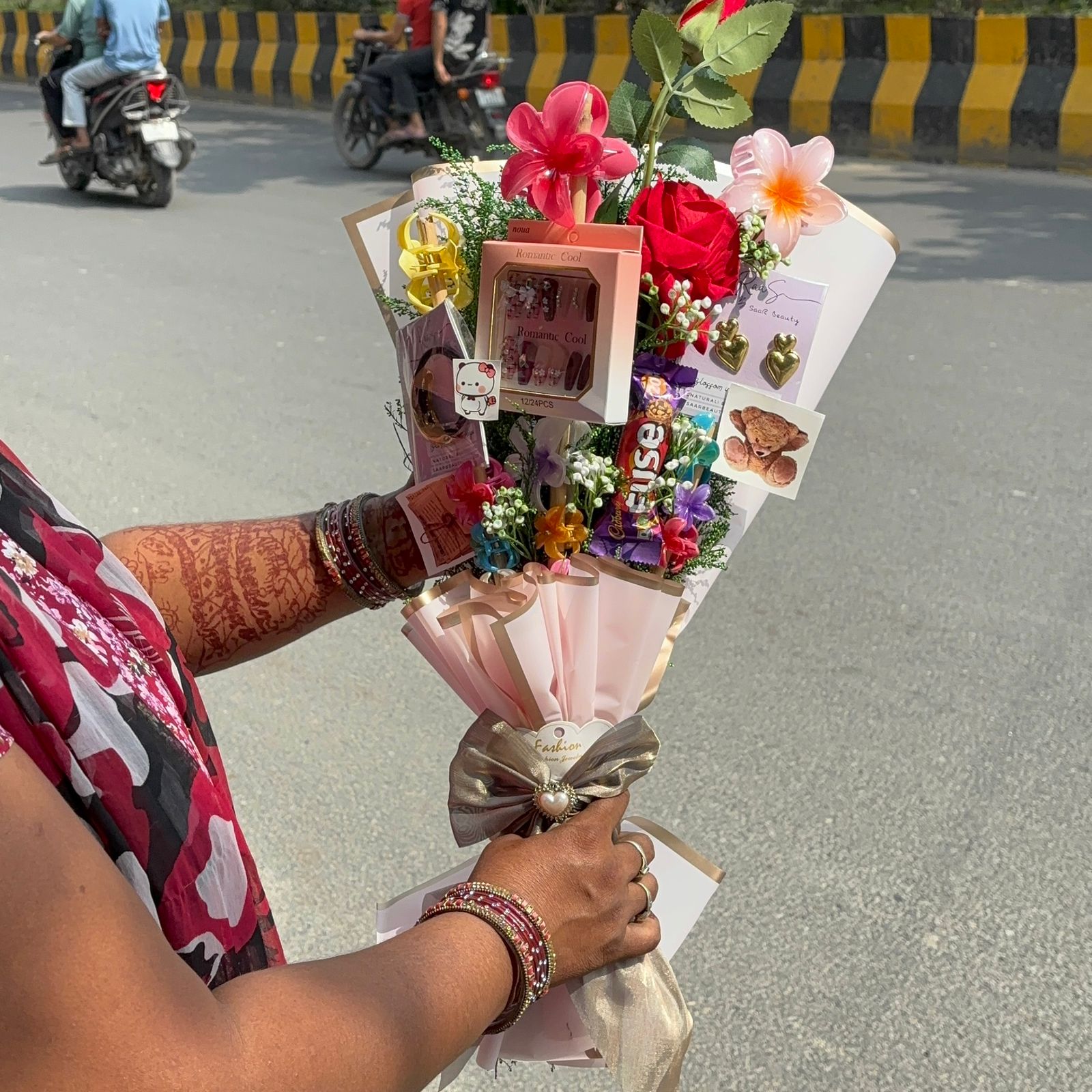 Person holding a bouquet of flowers with cards on a road. Pinterest-inspired Saar Beauty Forever Gift Bouquet with hair claws, nail box, and jewelry