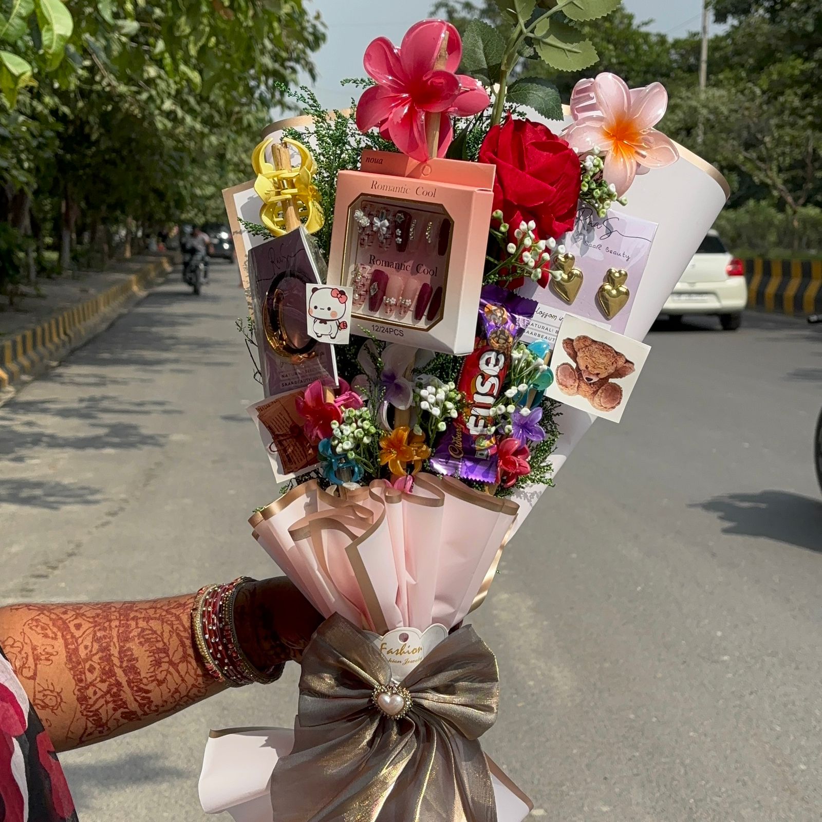 Bouquet with flowers and small gifts held by a person on a road. Pinterest-inspired Saar Beauty Forever Gift Bouquet with hair claws, nail box, and jewelry
