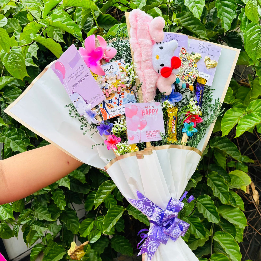 Bouquet with plush toys and flowers against a green leafy background Saar Beauty Limited Edition Birthday Accessories Bouquet – unique floral gift bouquet with hair clutchers, earrings, chocolates, and accessories for women and girl