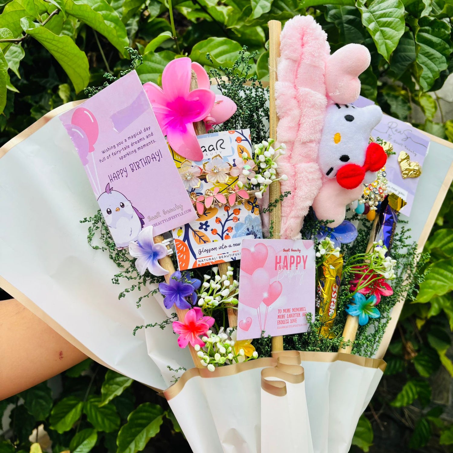 Bouquet with plush toys and cards against a green leafy background Saar Beauty Limited Edition Birthday Accessories Bouquet – unique floral gift bouquet with hair clutchers, earrings, chocolates, and accessories for women and girl