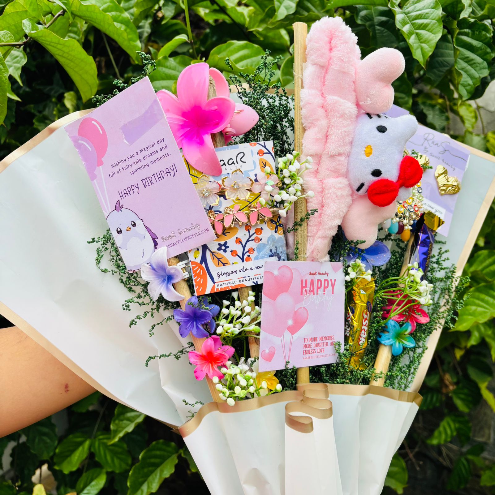 Bouquet with plush toys and cards against a green leafy background Saar Beauty Limited Edition Birthday Accessories Bouquet – unique floral gift bouquet with hair clutchers, earrings, chocolates, and accessories for women and girl